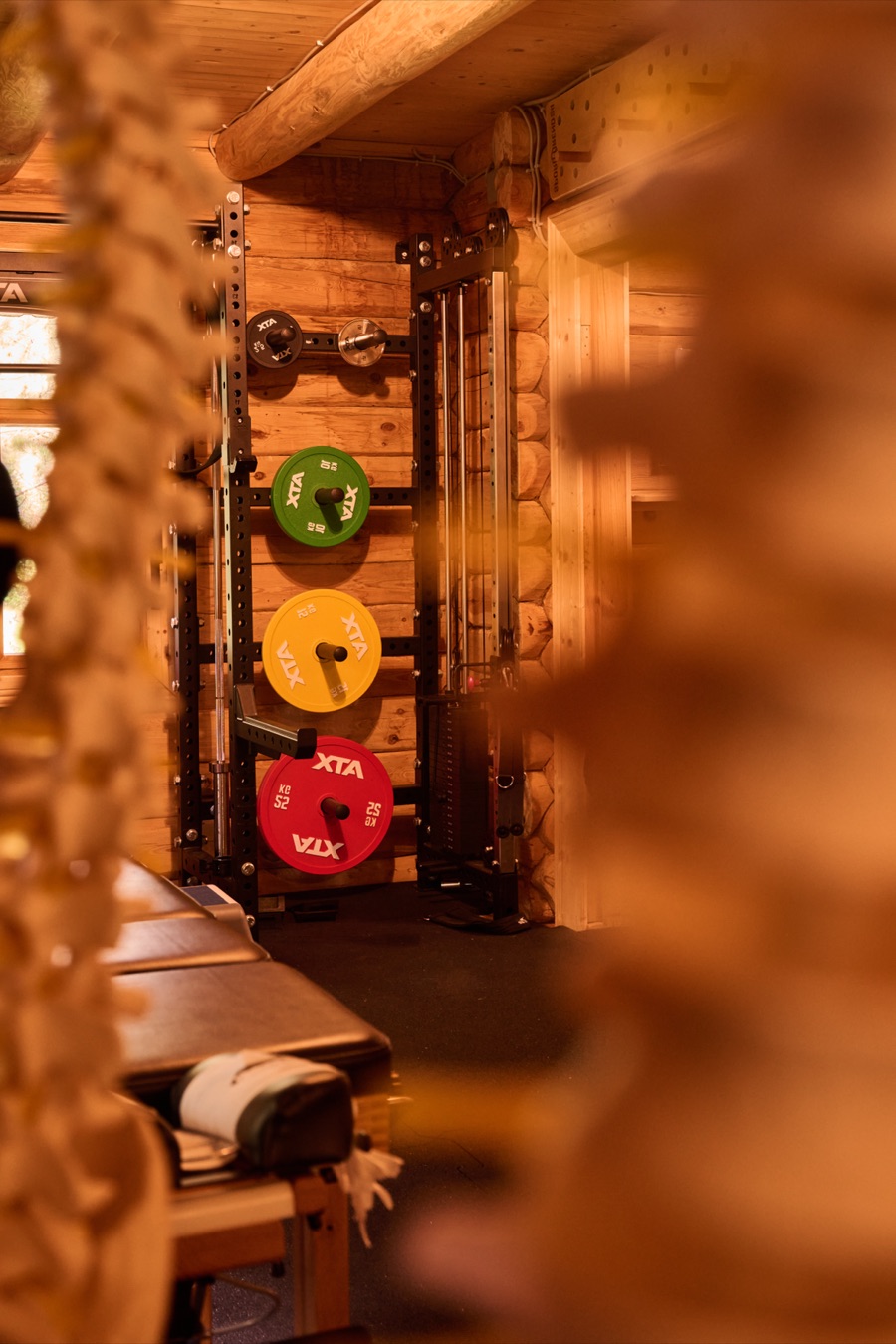 Blick an Holzschnitzereien vorbei auf ein Rack mit grüner, gelber und roter Hantelscheibe im unteren Raum.