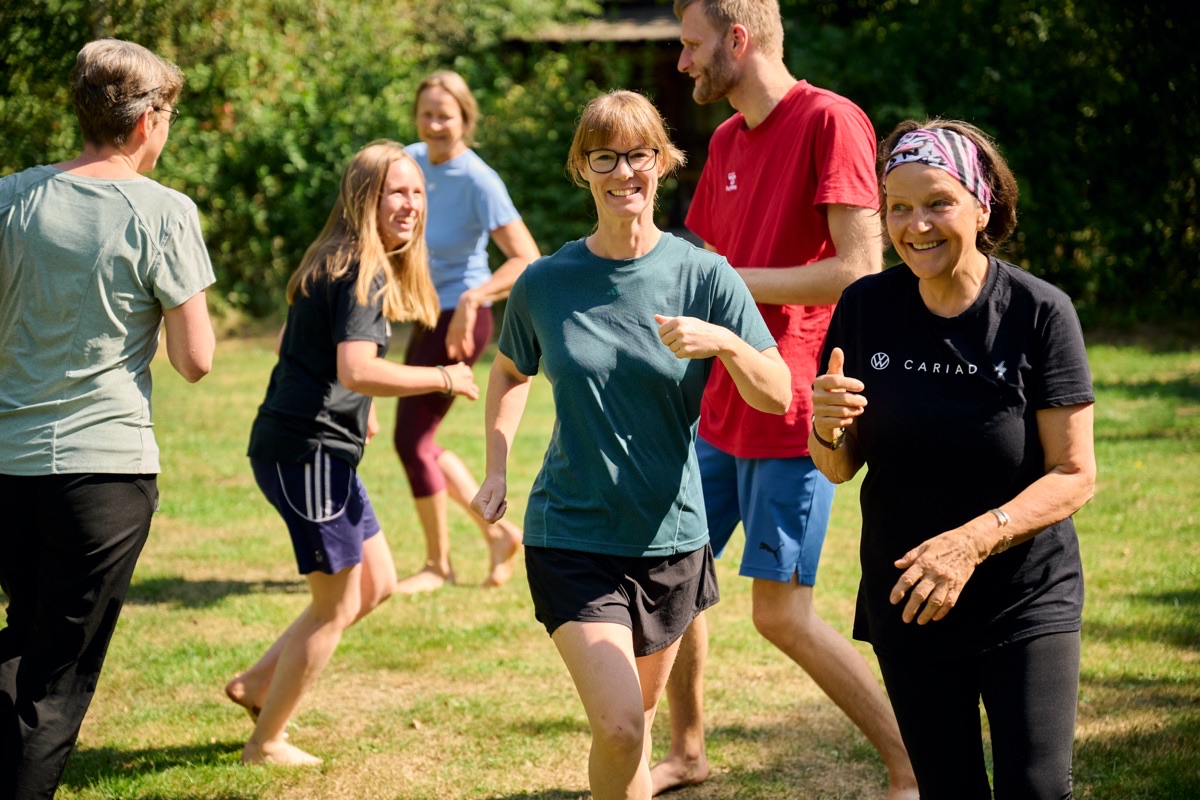 Gruppentraining auf der Wiese am Trainingshaus: mehrere Menschen lachen und bewegen sich gemeinsam.
