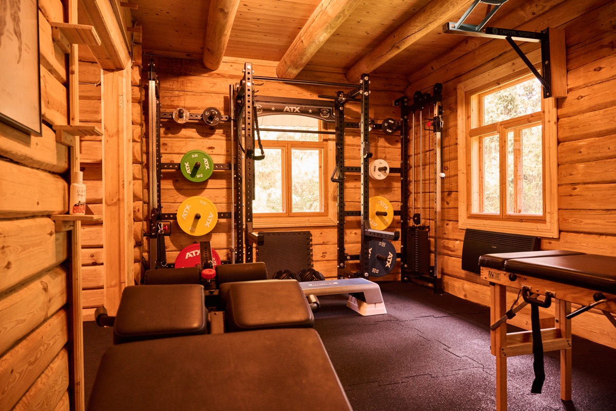 Der untere Trainingsraum mit Holzwänden, Rack, Hantelscheiben und Behandlungsliege.
