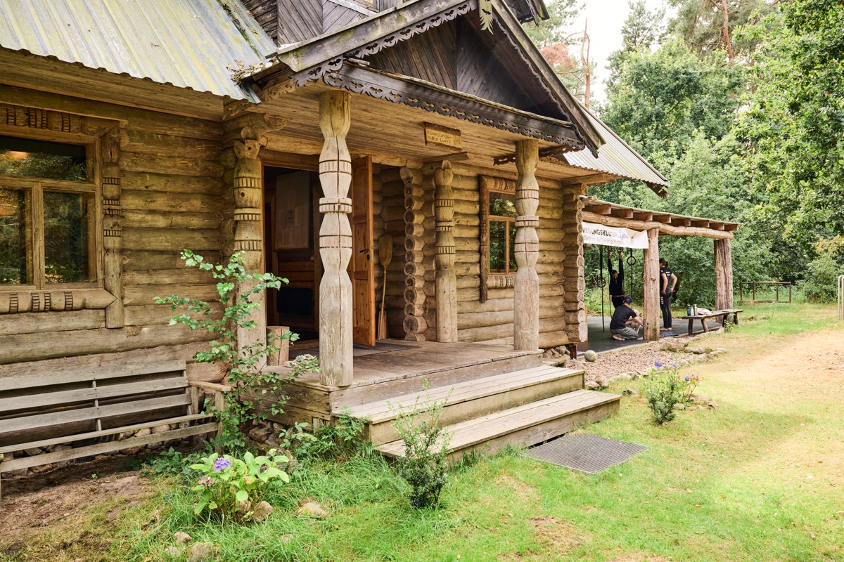 Die Veranda des Trainingshauses: ein Holzhaus mit geschnitzten Säulen, Stufen und Pflanzen davor.